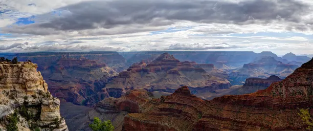 Layered red rock buttes in the Grand Canyon beneath dark, heavy storm clouds with small patches of blue sky.