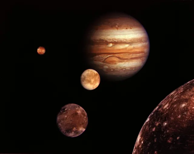 Jupiter with its banded clouds and Great Red Spot, beside four of its moons arranged against black space.