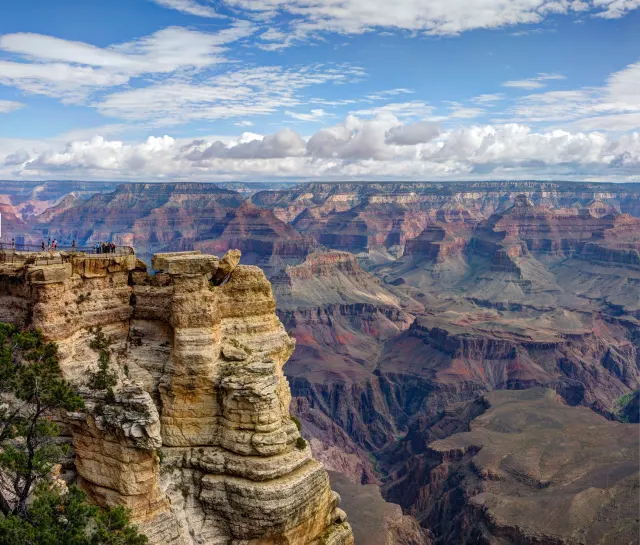 Sandstone outcrop with a lookout above the Grand Canyon's red buttes under a blue sky with white clouds.